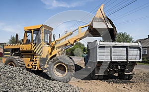 Yellow loader delivering stone gravel into truck during road construction works. The stones for the road. Unloading