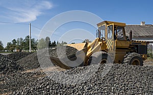 Yellow loader moving with uploaded bucket with stone gravel during road construction works. The stones for the road