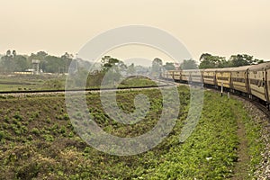 A yellow long Indian railway diesel locomotive passenger train in countryside of dooars area on curvy stretch of track with