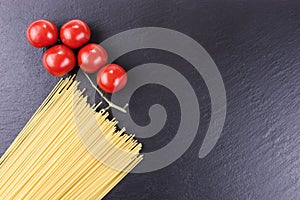 Yellow raw spaghetti and cherry tomatoes on black slate plate