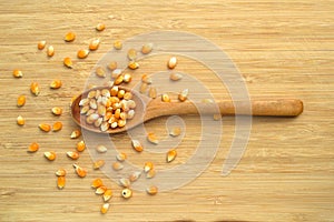 Yellow maize corn kernels ready for making popcorn, on bamboo cutting board and in wooden spoon