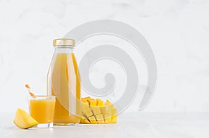 Yellow mango juice in glass bottle mock up with straw, wine glass, fruit slice on white wood table in light interior, template.