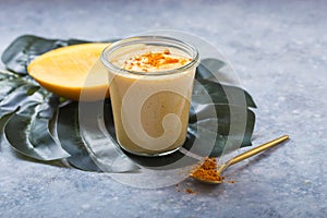 Yellow mango yogurt or smoothie on grey background. Turmeric Lassie or lassi in glass