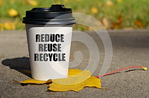 On a yellow maple leaf there is a cup of coffee on which is written - reduce, reuse, recycle
