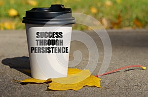 On a yellow maple leaf there is a cup of coffee on which is written - Success through persistence