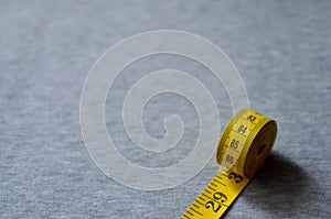 Yellow measuring tape lies on a gray knitted fabric