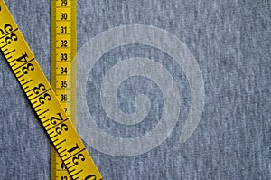 Yellow measuring tape lies on a gray knitted fabric