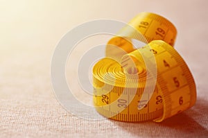 Yellow measuring tape with numerical indicators in the form of centimeters or inches lies on a gray knitted fabric. Concept indus