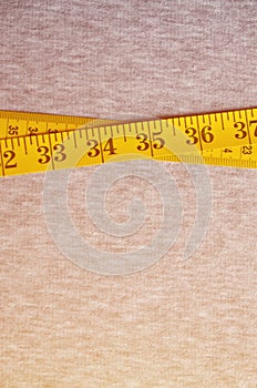 Yellow measuring tape with numerical indicators in the form of centimeters or inches lies on a gray knitted fabric. Concept indus