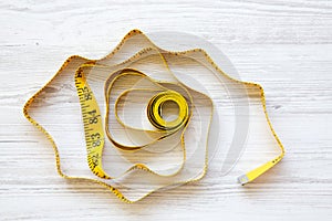 Yellow measuring tape on white wooden background, from above.