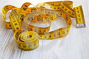 Yellow measuring tape on white wooden background, side view.