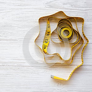 Yellow measuring tape on a white wooden background, top view. Space for text