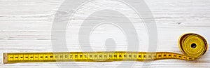 Yellow measuring tape on white wooden table, top view. From above, flat lay.