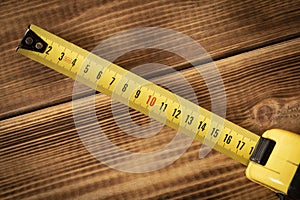 Yellow measuring tape on a wooden background. Close-up