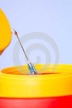 Yellow medical disposal waste box, syringe needle with red drop on the tip