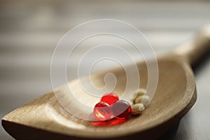 Yellow medical pills and red vitamins a wooden spoon, closeup on the table, side view