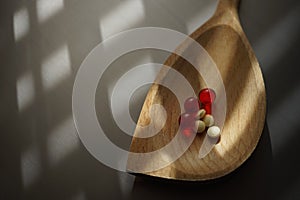 Yellow medical pills and red vitamins in wooden spoon. Top view on the sunny table with copy space