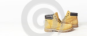 Yellow men`s work boots from natural nubuck leather on wooden white background. Trendy casual footwear, youth style. Concept of