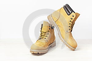 Yellow men`s work boots from natural nubuck leather on wooden white background. Trendy casual shoes, youth style. Concept of