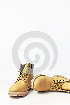 Yellow men`s work boots from natural nubuck leather on wooden white background. Trendy casual shoes, youth style. Concept of