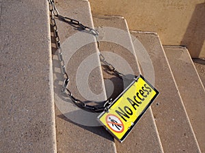 Yellow metal no access sign on a chain on concrete steps with no pedestrian symbol