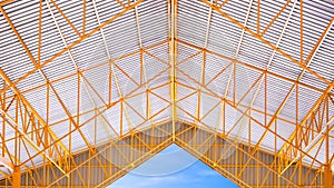 Yellow metal roof beams and aluminum corrugated tile roof of industrial building with blue sky background