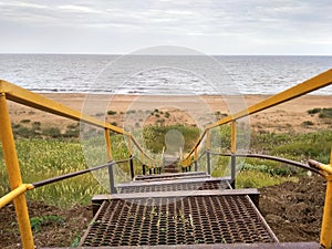 Yellow metal staircase to the sea.Beach with high grass.