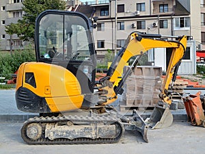 Yellow mini excavator on tracks for small construction works in hard-to-reach places or on narrow city streets