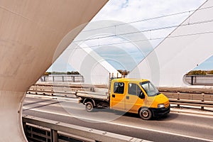 Yellow mini truck speeding over modern bridge, used in intra-city low tonnage cargo delivery photo