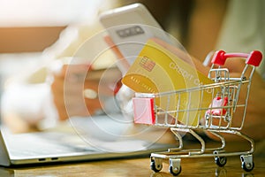 Yellow mock up banking card or credit card in shopping cart on wooden table background with woman using smartphone and credit card