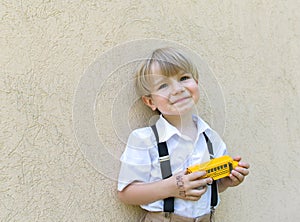 Yellow model of a toy school bus in the hands of a cheerful cute schoolboy in a white shirt