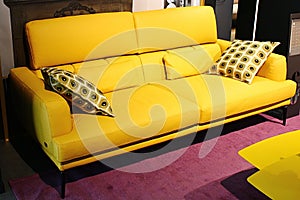 Žlutá moderní pohodlná kožená pohovka se dvěma černými a žlutými dekoračními polštáři v rohu, jak je zobrazeno Ego Company