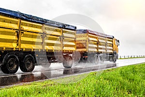 Yellow modern grain truck transporting grain in rainy weather on the highway, in the background. Slippery road