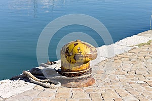 A yellow mooring bollard with a mooring rope on the harbor pier Italy, Europe