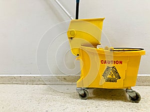 Yellow mop bucket with wheels on the white marble floor