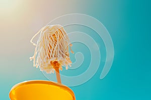Yellow mop drenched with water stands erect against a vibrant blue sky background