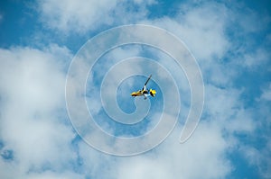 A yellow motorized hang glider with a propeller soars in the blue sky