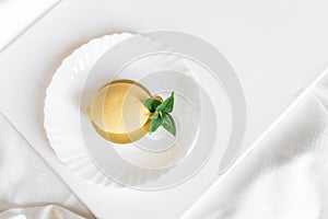 Yellow mousse cake in the form of a lemon lies on a white plate with a spoon on a light background.