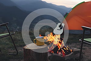 Yellow mug with hot drink on wooden stump near bonfire outdoors. Camping season