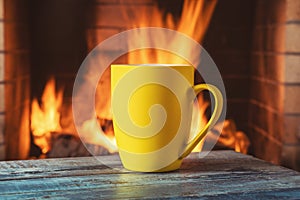 Yellow mug of tea or coffee before a a cozy fireplace, in a country house, autumn or winter holidays