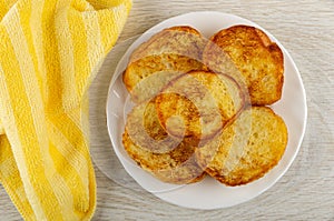 Yellow napkin, white plate with toasted slices of bread on table. Top view