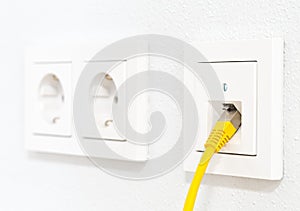 Yellow network cable in wall outlet for office or private home lan ethernet connection with power outlets flat view on white