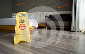 A yellow `NO ENTRY` sign place on the floor in hotel room. While cleaning