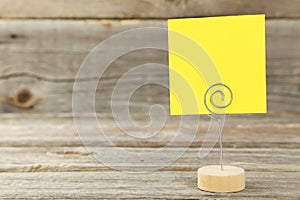 Yellow note paper on a holder on grey wooden background.