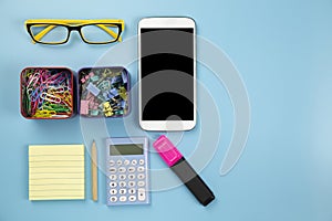 Yellow notebook mobile phone calculator and hilight marker glasses clip on blue background pastel style with copyspace flatlay