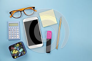 Yellow notebook mobile phone calculator and hilight marker orange glasses on blue background pastel style with copyspace flatlay