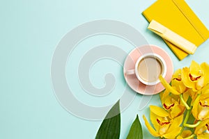 Yellow notebook, pen, cup of coffee, yellow flowers on blue background