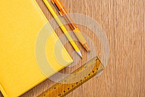 Yellow notebook, yellow pen, yellow pencil and yellow ruler on a wooden table surface. Stationery of the same color. Office