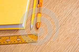 Yellow notebook, yellow pen, yellow pencil and yellow ruler on a wooden table surface. Stationery of the same color. Office