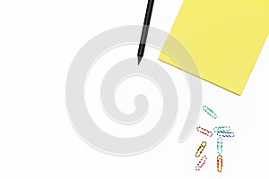 Yellow Notepad, black pencil, and colored paper clips on a white background. Minimal business concept. Flat law.